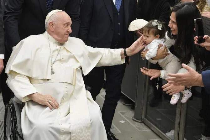 Le pape François, assis dans un fauteuil roulant, salue un enfant pendant l'audience générale du pape au Vatican, le 25 janvier 2023. | Vatican Media / 